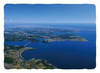 晴天の都市の航空写真。深く入り込んだ湾と、湾を渡る大きな橋、そして海岸沿いに広がる市街地の景色